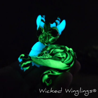 A glowing clay dragon in a wood stump against a blurred background with greenery. Text says Wicked Winglings