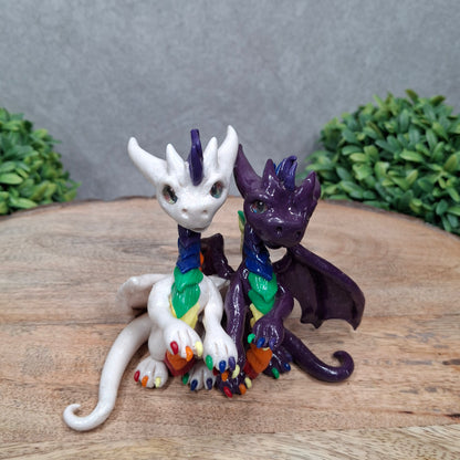 a dragon pair with rainbow accents against a wood surface with greenery