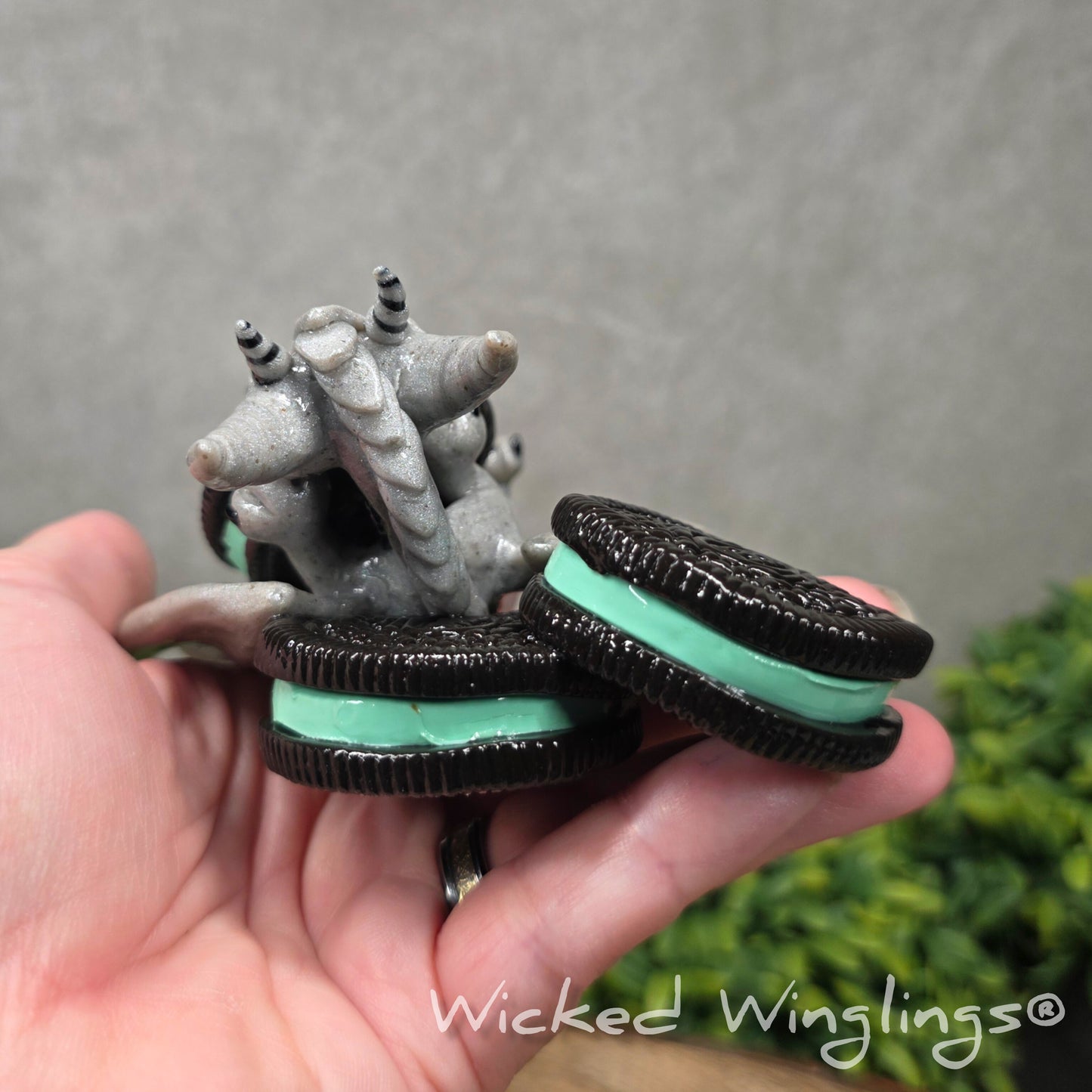 Back view of A hand holding a clay dragon with cookies with a Wicked Winglings® watermark.