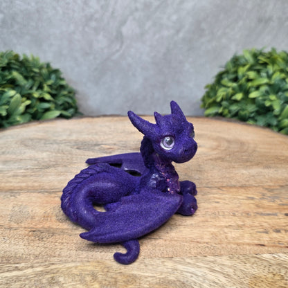 A flocked clay dragon sculpture on a wood surface with greenery.