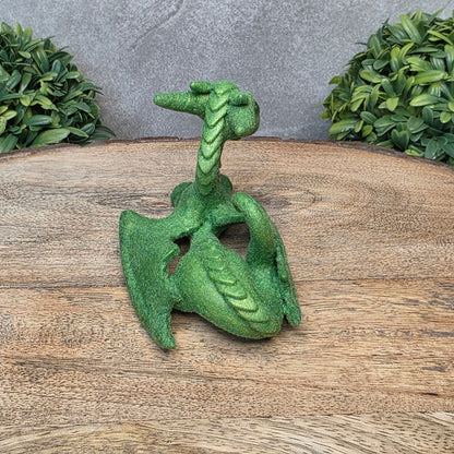 A flocked clay dragon sculpture on a wood surface with greenery.