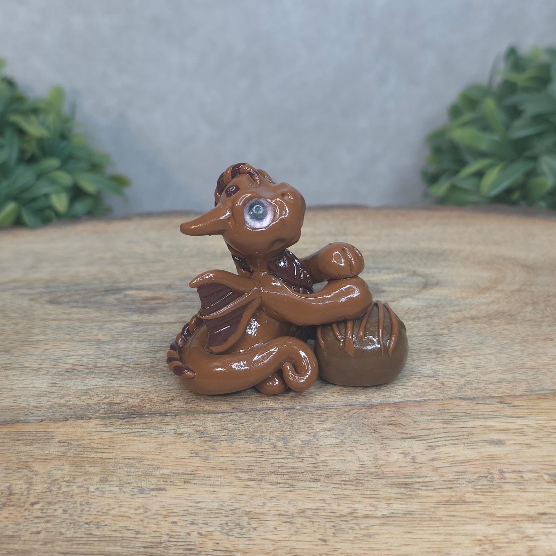 A baby polymer clay dragon with a chocolate truffle against a blurred background