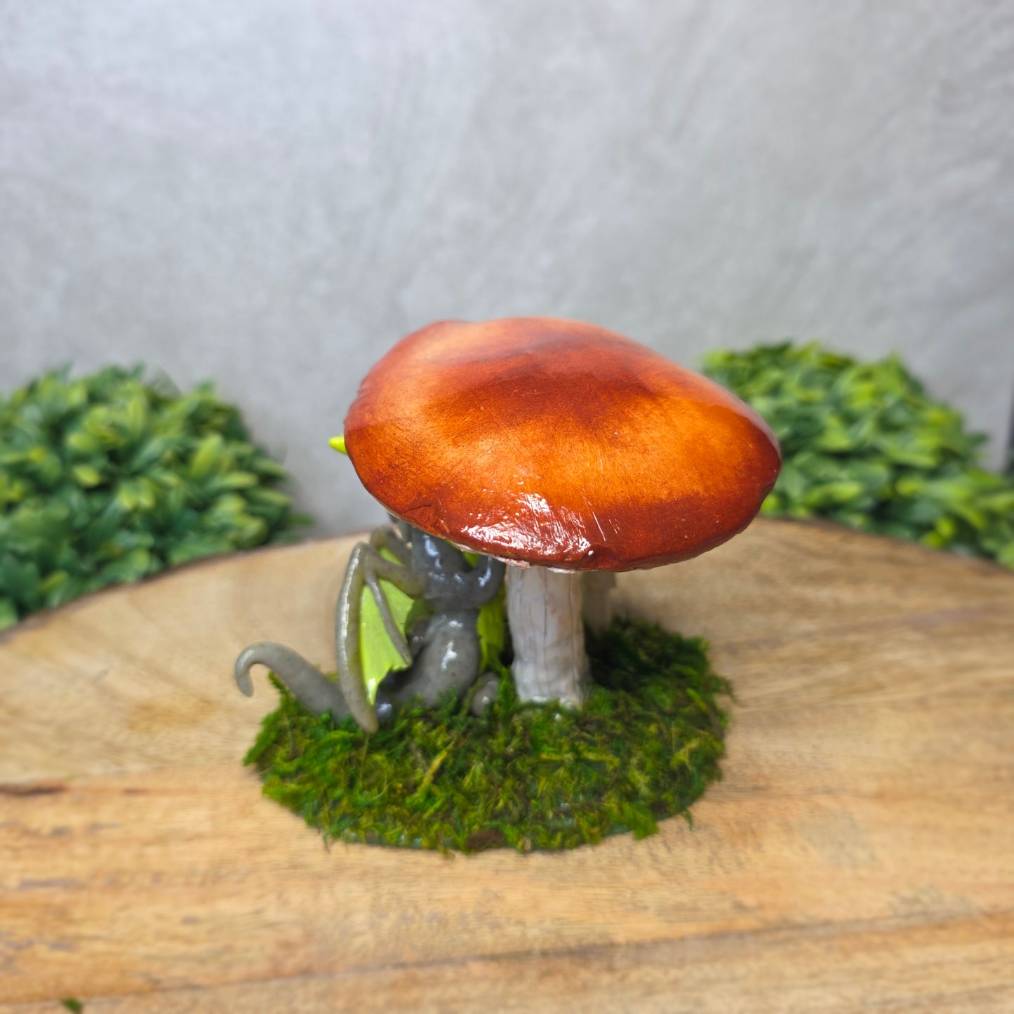 A clay dragon on a wooden surface with greenery.