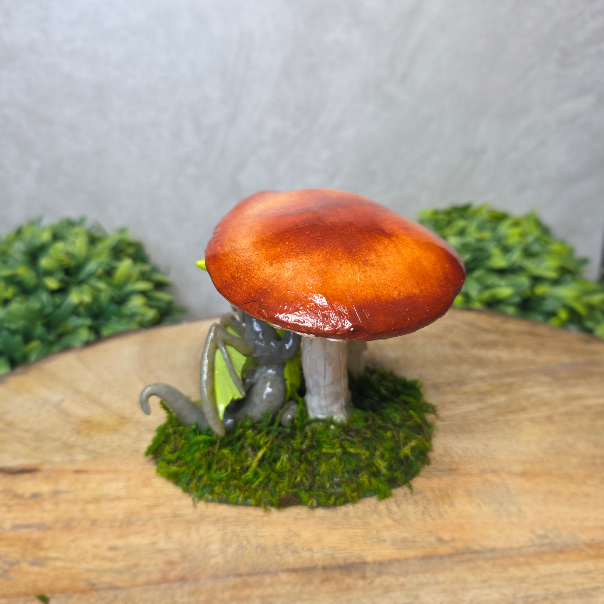 A clay dragon on a wooden surface with greenery.
