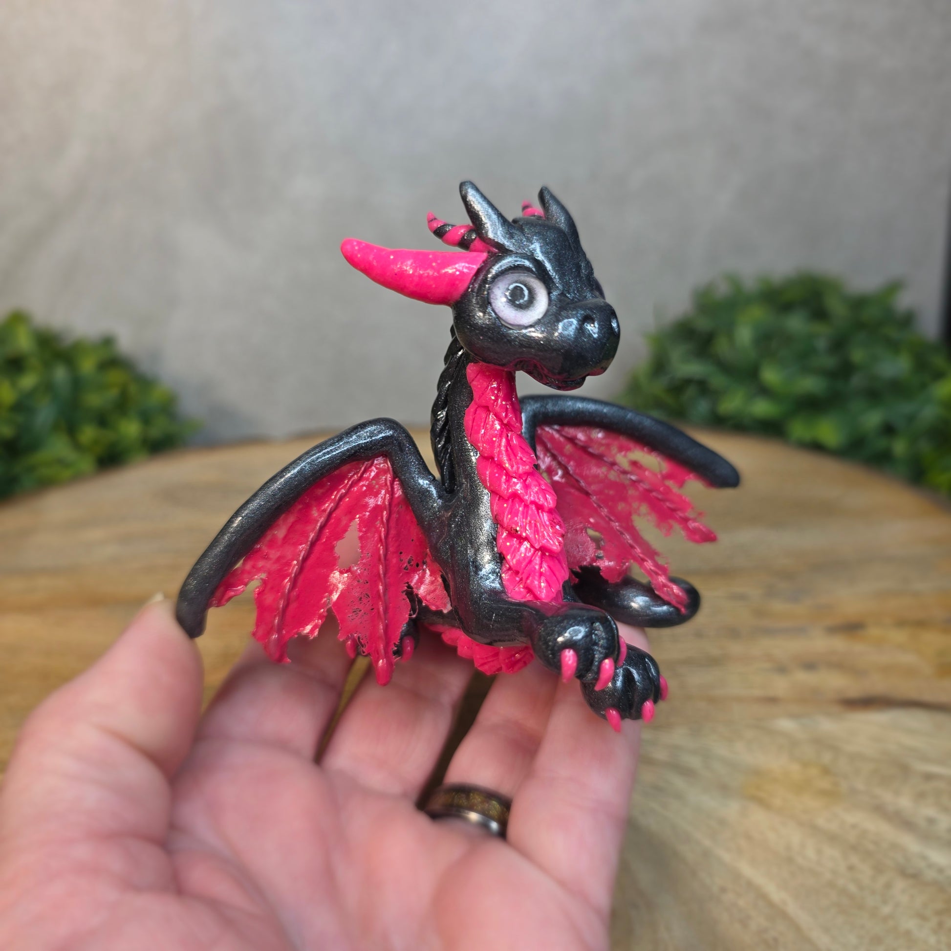 A hand holding a graphite and pink clay dragon against a blurred wood surface