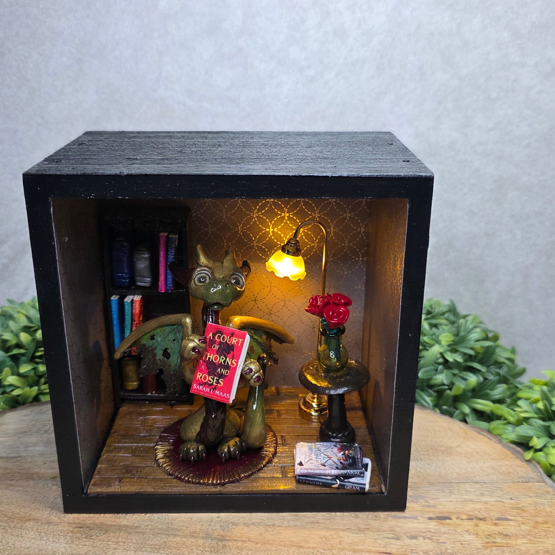 Book nook with dragon on a wood surface with greenery