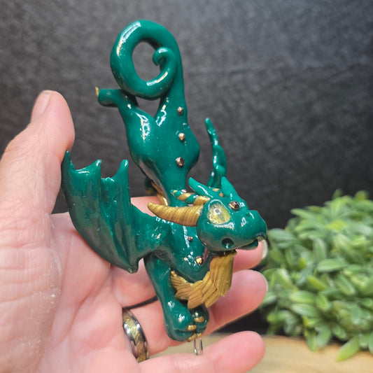 Hand holding a green and gold clay dragon accented with crystals