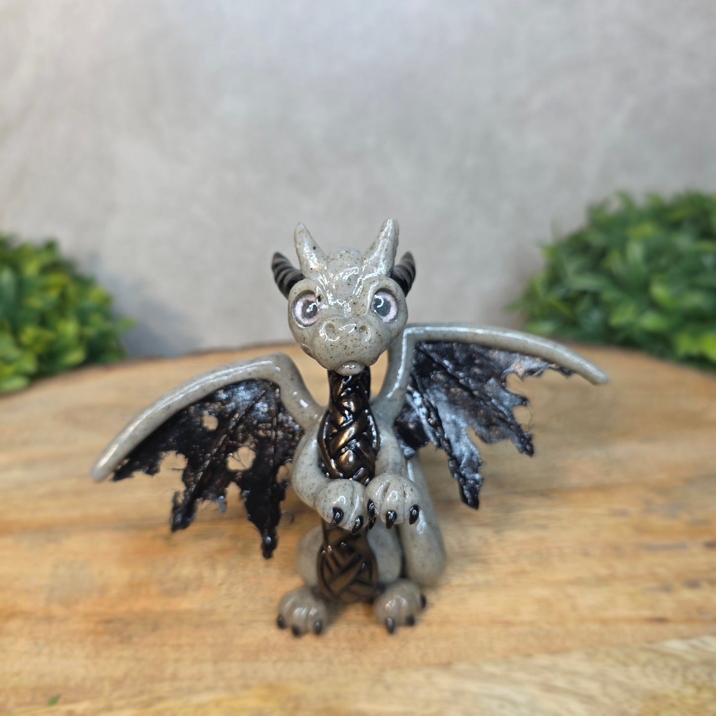 A clay dragon figurine on a wooden surface with a blurred green plant in the background