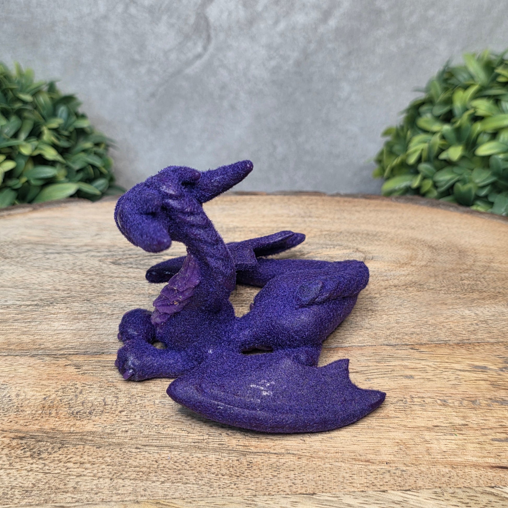 A flocked clay dragon sculpture on a wood surface with greenery.