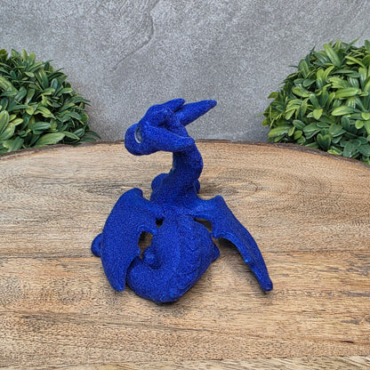 A flocked clay dragon sculpture on a wood surface with greenery.