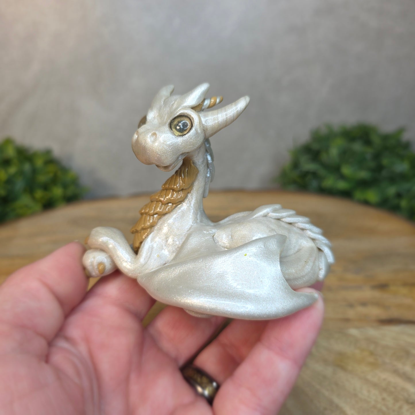 A hand holding a pearl and tan clay dragon against a blurred wood surface