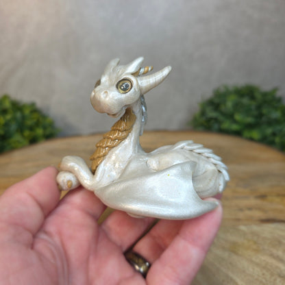 A hand holding a pearl and tan clay dragon against a blurred wood surface