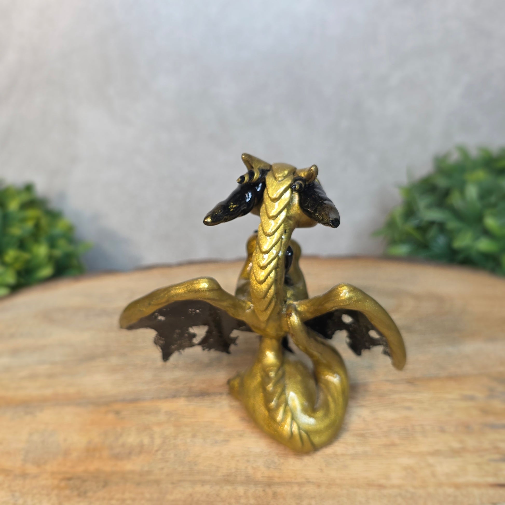 A clay dragon figurine on a wooden surface with a blurred green plant in the background