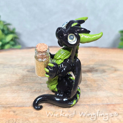 A clay dragon with a potion bottle on a wood surface. Text reads Wicked Winglings.
