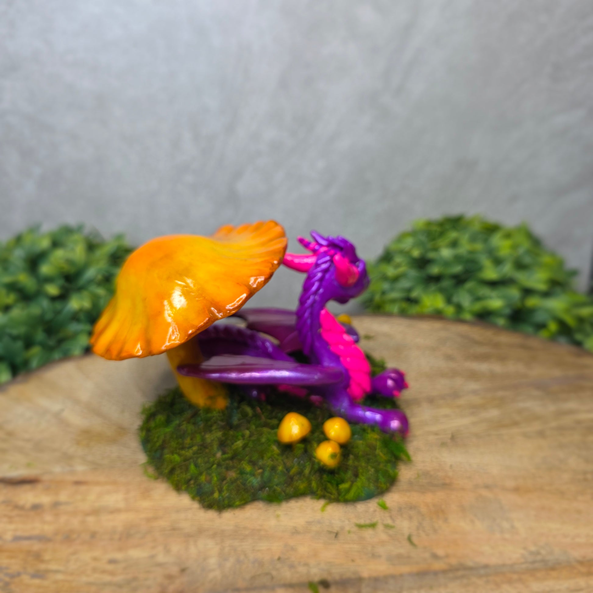 Purple dragon figurine with a yellow mushroom on a wooden surface with greenery
