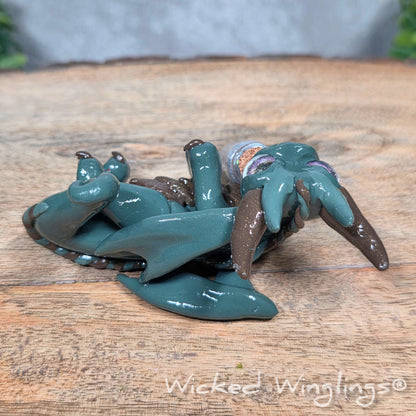 A clay dragon with a potion bottle on a wood surface. Text reads Wicked Winglings.