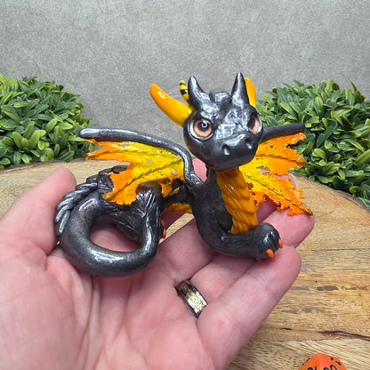 Hand holding a clay dragon against a wood surface with greenery.