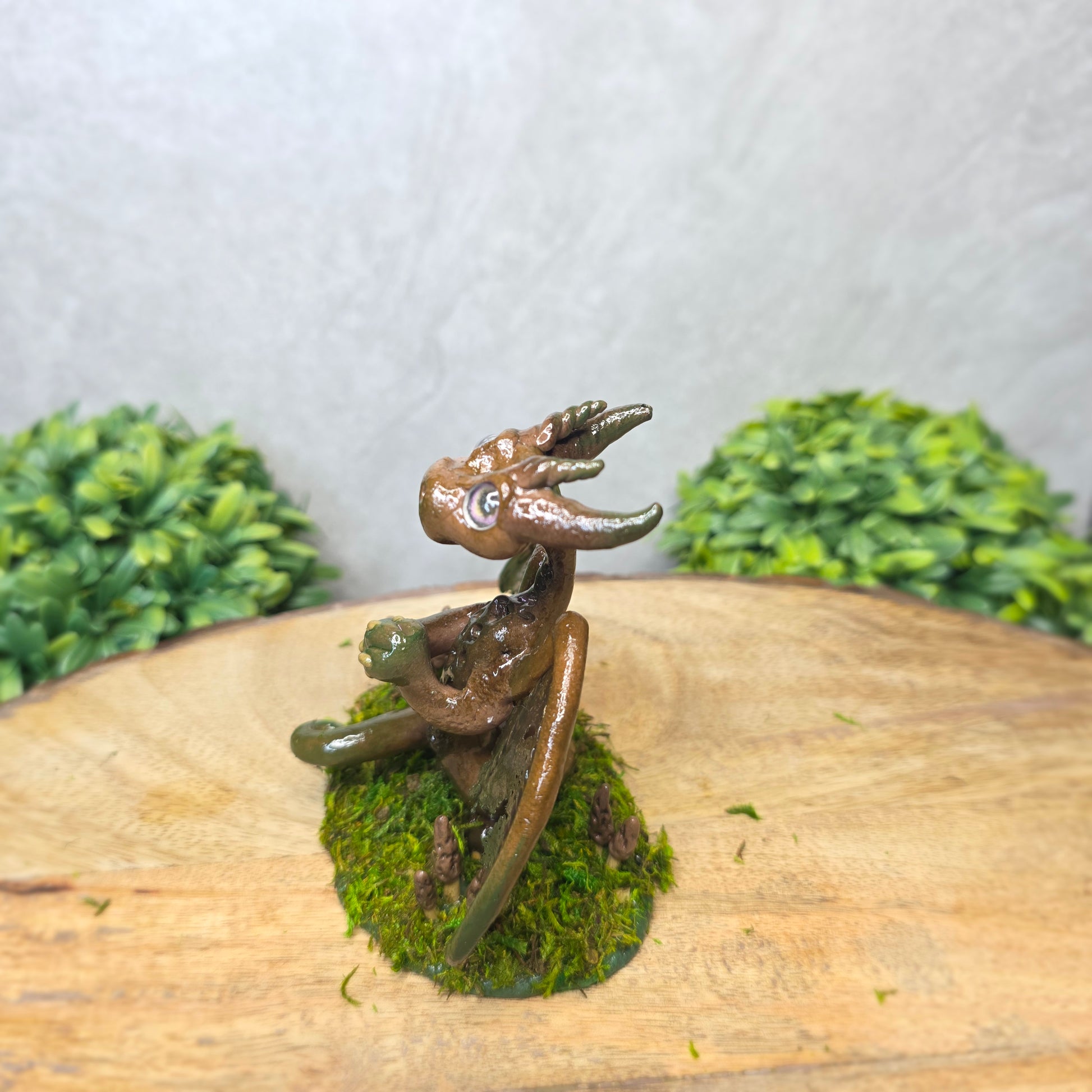 Small dragon figurine on a piece of wood with greenery in the background