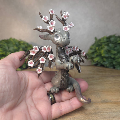Hand holding a gray colored dragon with cherry blossom accents