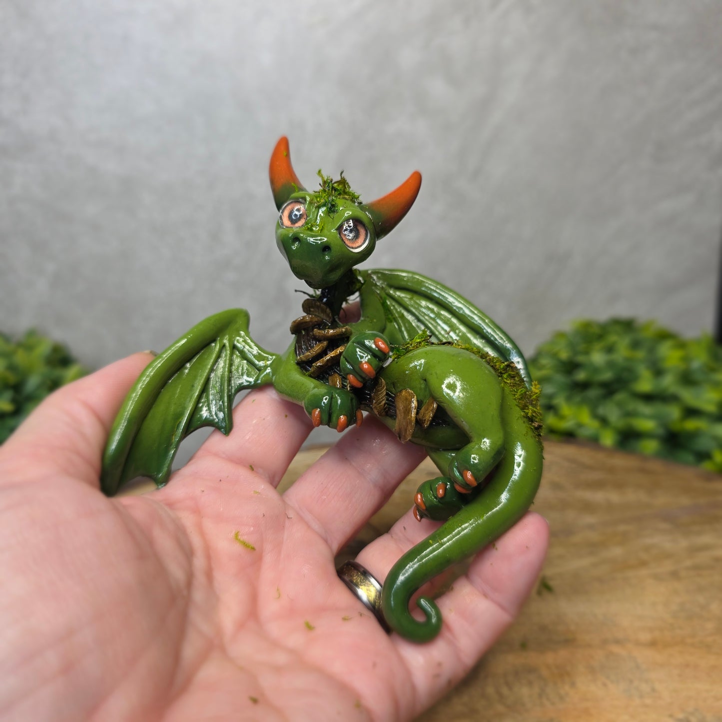 A hand holding a green clay dragon against a blurred background