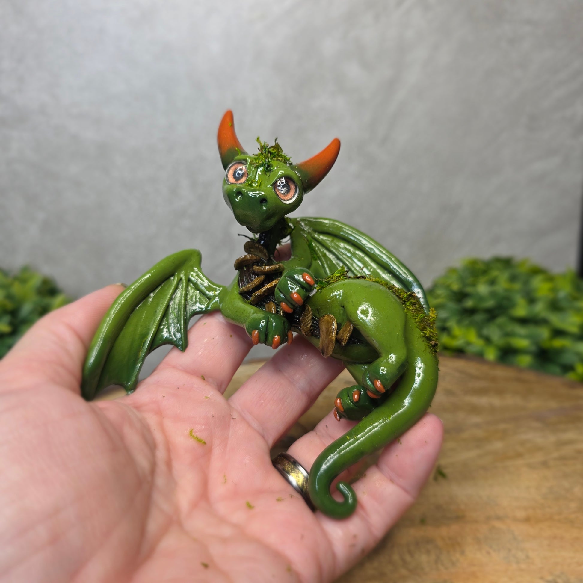 A hand holding a green clay dragon against a blurred background