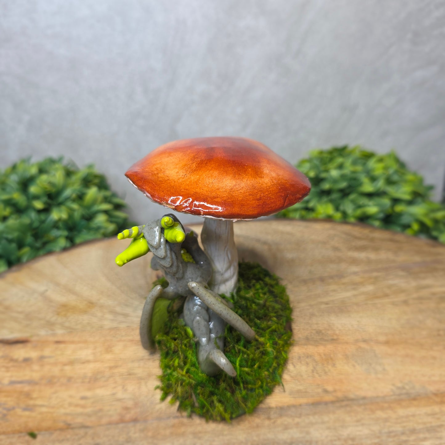 Back view of a clay dragon on a wooden surface with greenery.