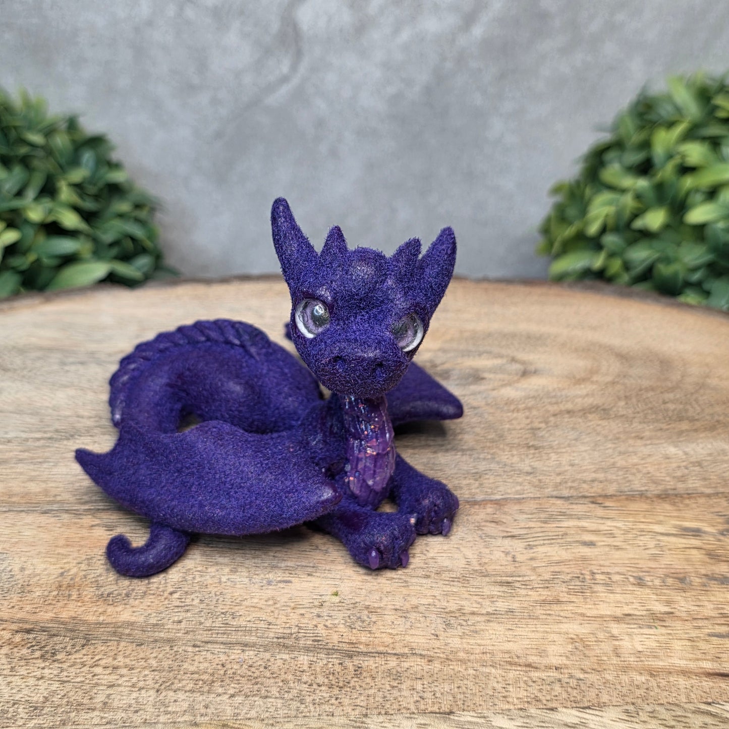 A flocked clay dragon sculpture on a wood surface with greenery.