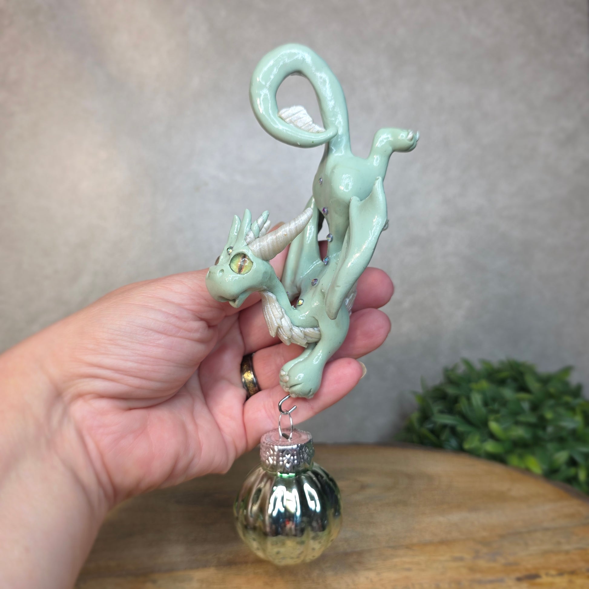 Hand holding a small aqua dragon with glass ornament against a blurred background