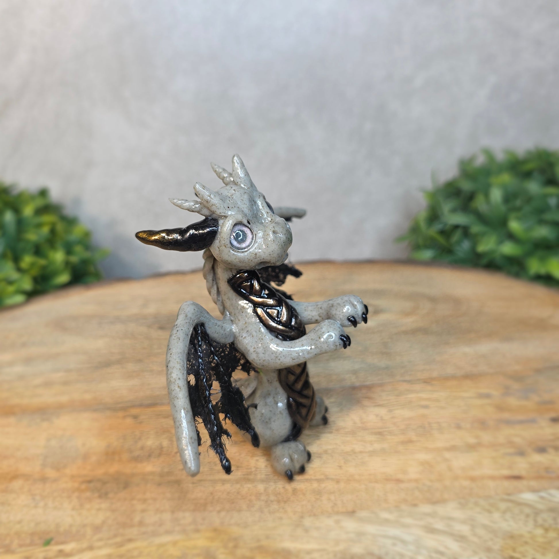 A clay dragon figurine on a wooden surface with a blurred green plant in the background