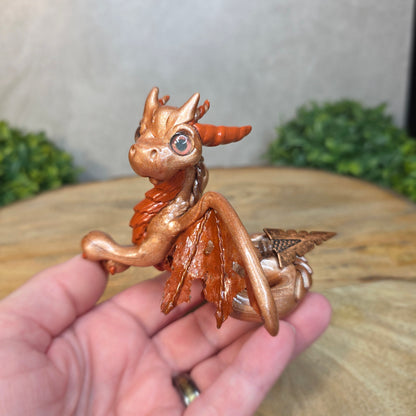 Copper dragon figurine held in a hand with a blurred background