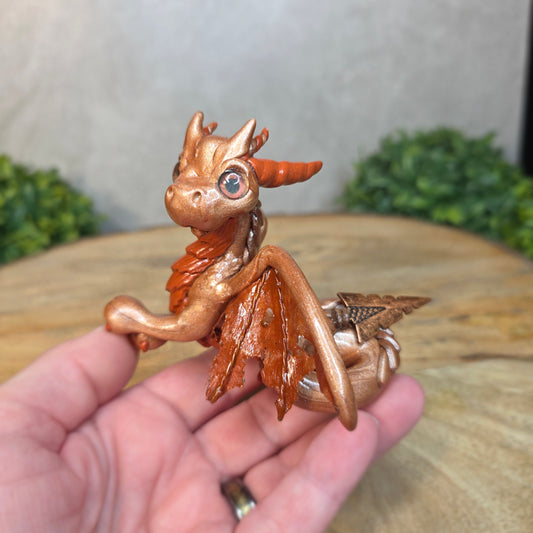 Copper dragon figurine held in a hand with a blurred background