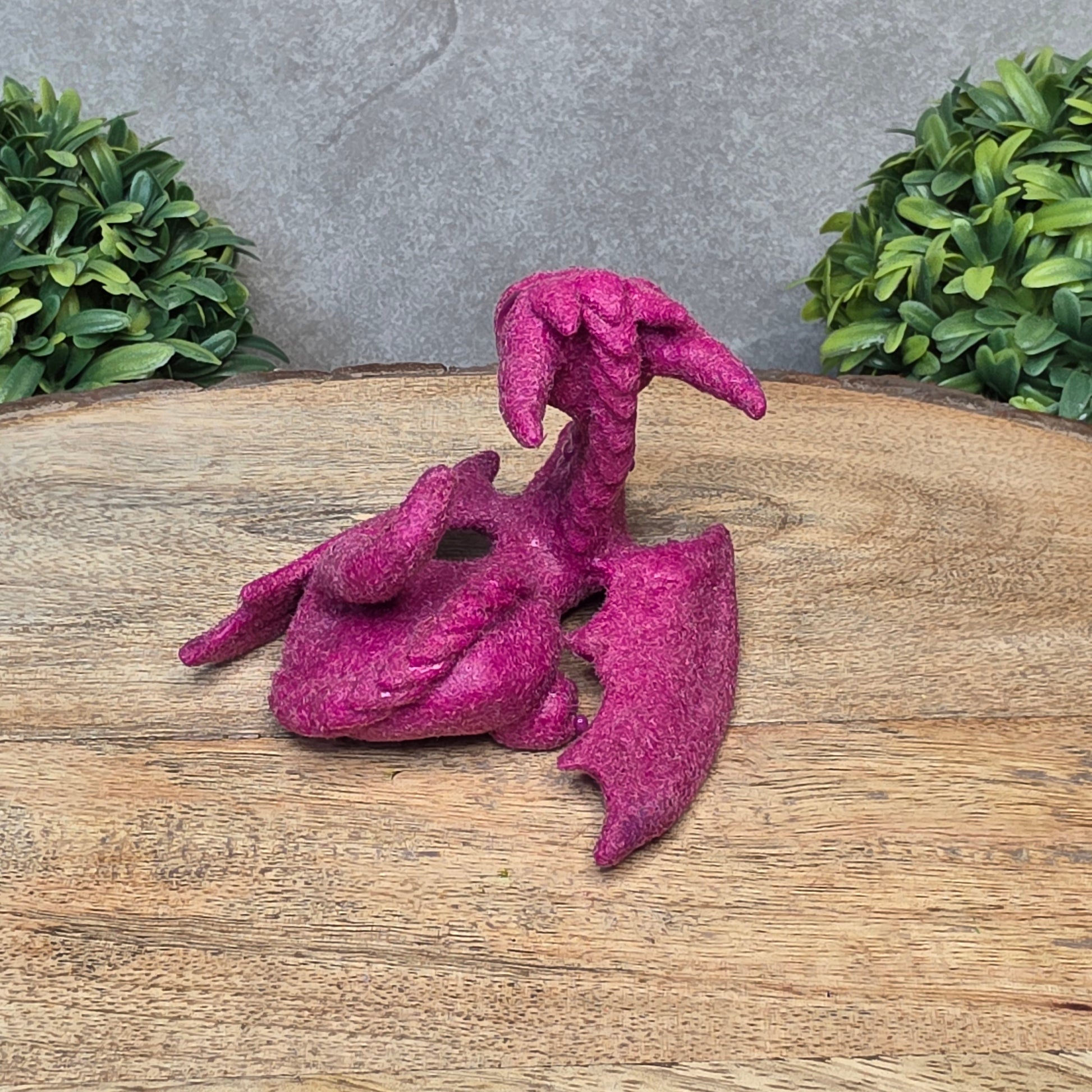 A flocked clay dragon sculpture on a wood surface with greenery.