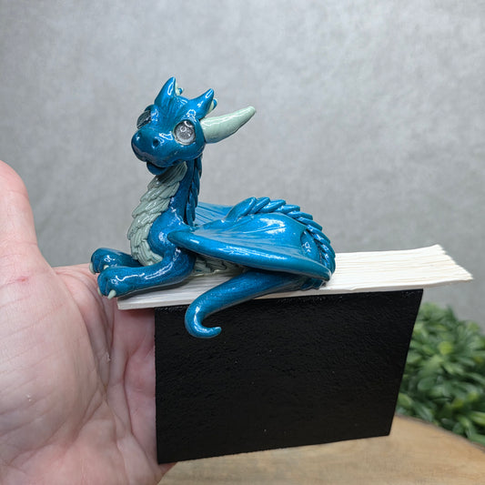 Hand holding a dragon book insert against a background with greenery