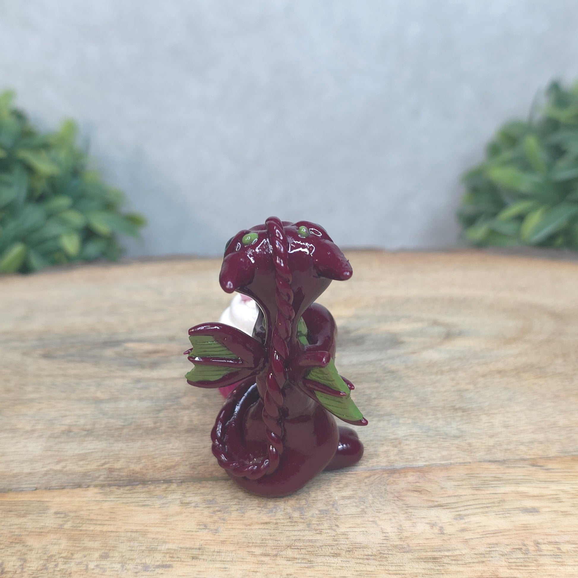 A baby polymer clay dragon with a cupcake against a blurred background