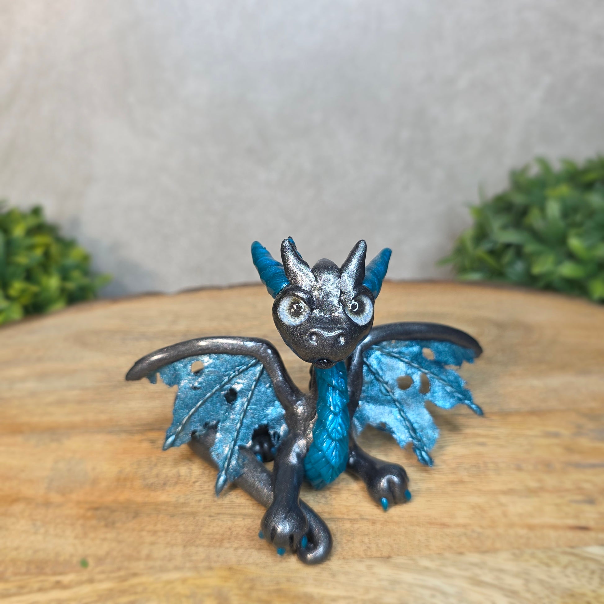 A graphite and blue clay dragon against a blurred wood surface