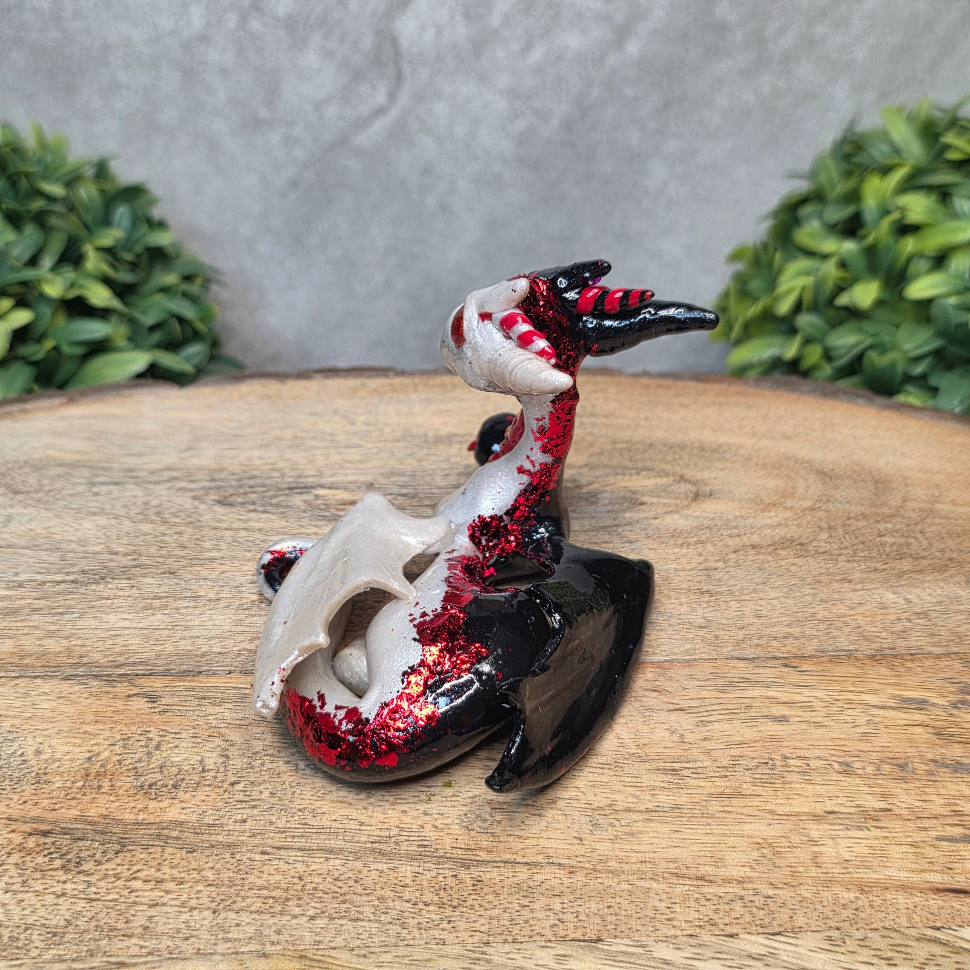 A 2 toned clay dragon sculpture on a wood surface with greenery.