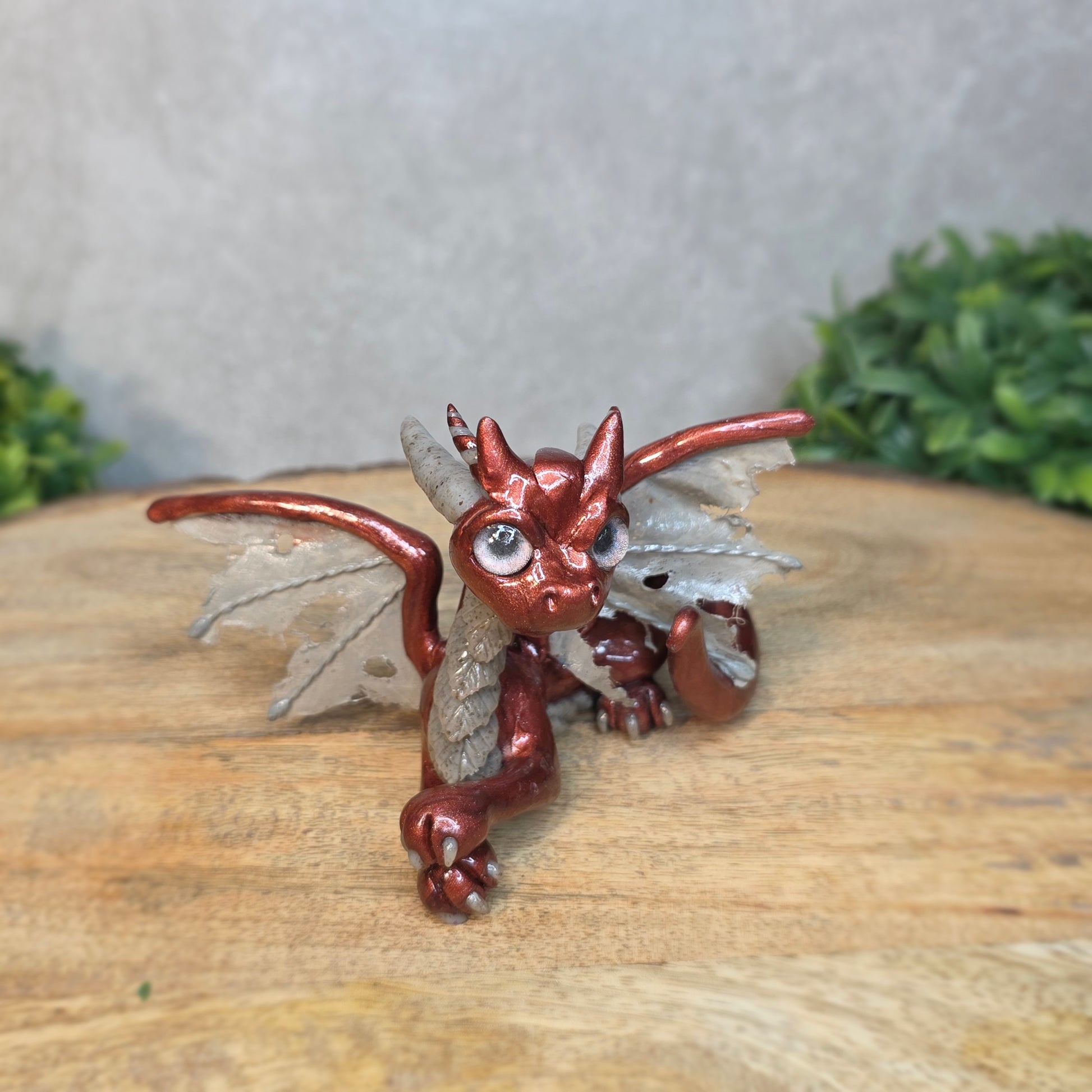 A bronze and gray clay dragon against a blurred wood surface