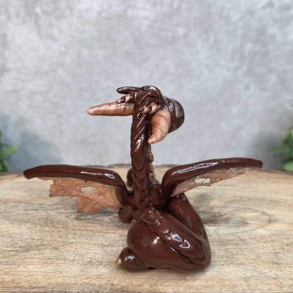 A brown and copper clay dragon against a blurred wood surface