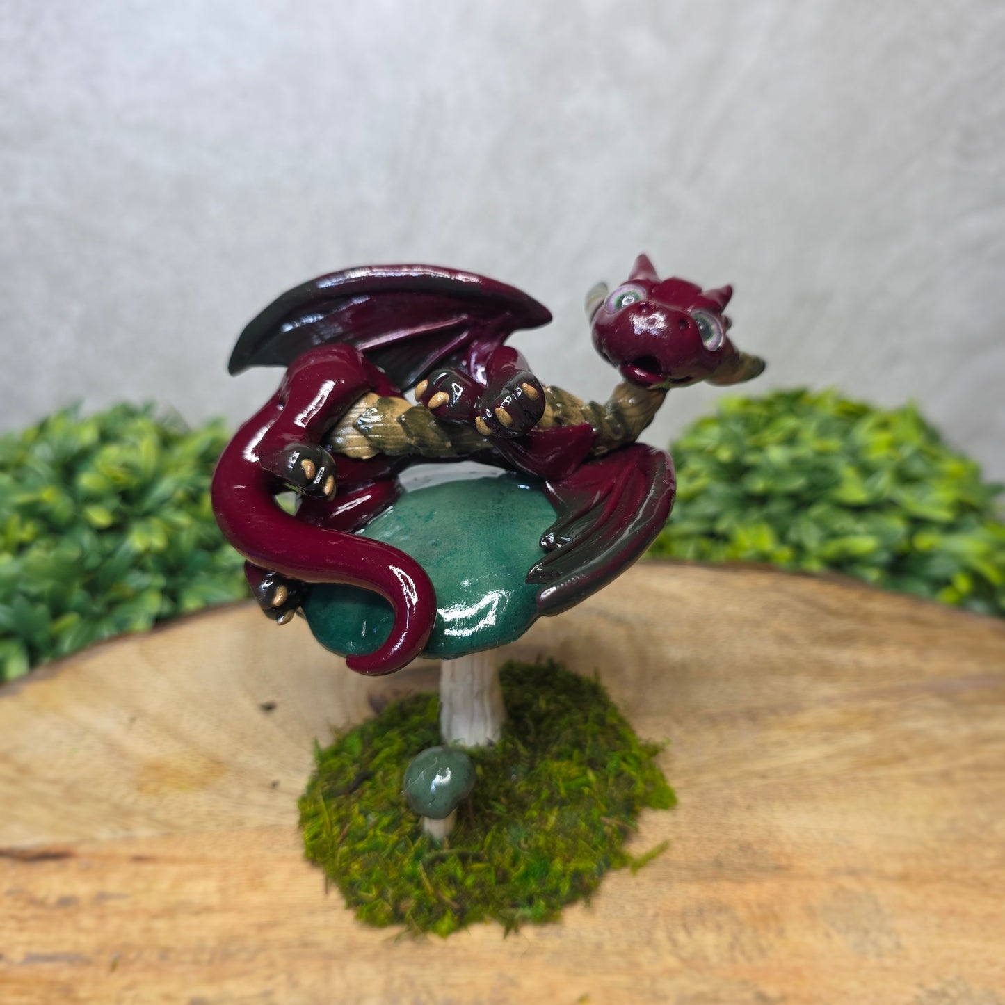 Small dragon figurine on a wooden surface with greenery