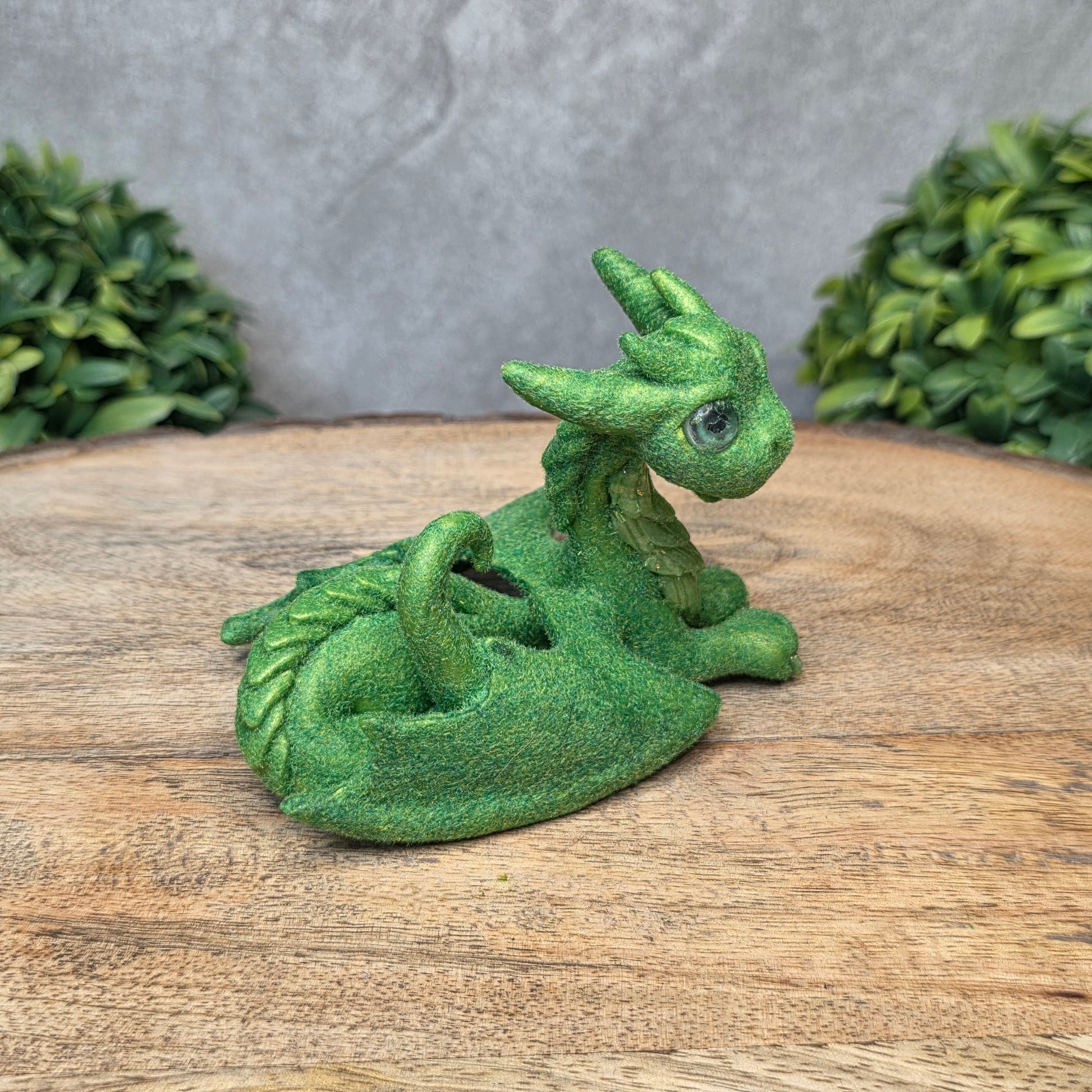 A flocked clay dragon sculpture on a wood surface with greenery.
