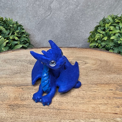 A flocked clay dragon sculpture on a wood surface with greenery.