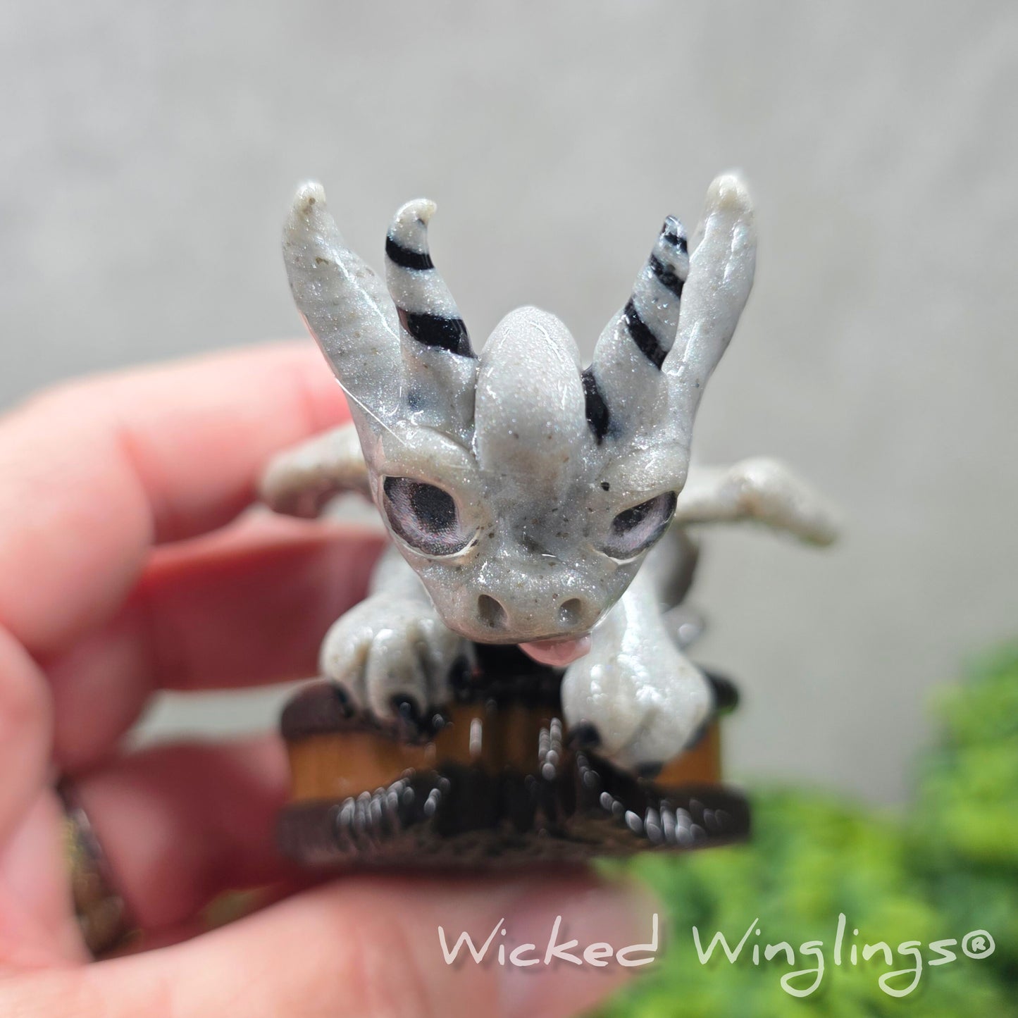 Top view of a hand holding a clay dragon with a cookie with a Wicked Winglings® watermark.