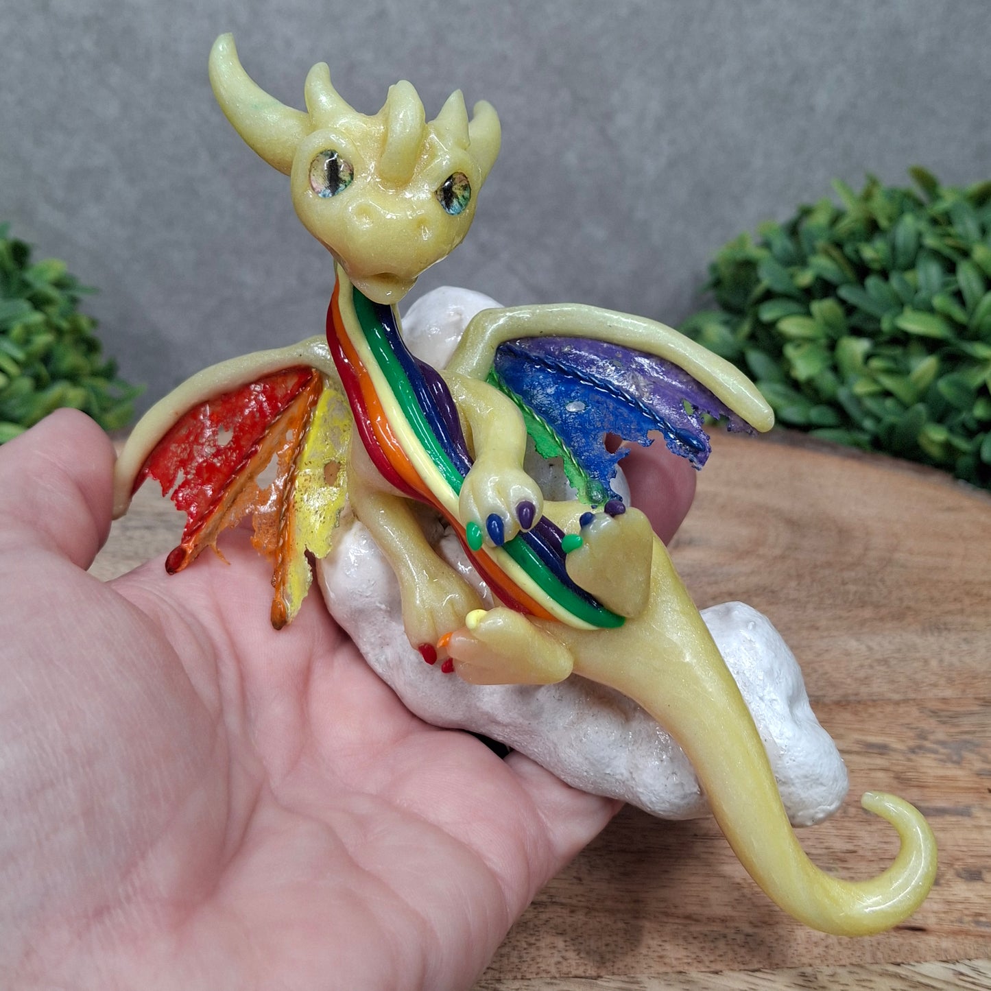 Hand holding a yellow dragon with rainbow accents on a cloud