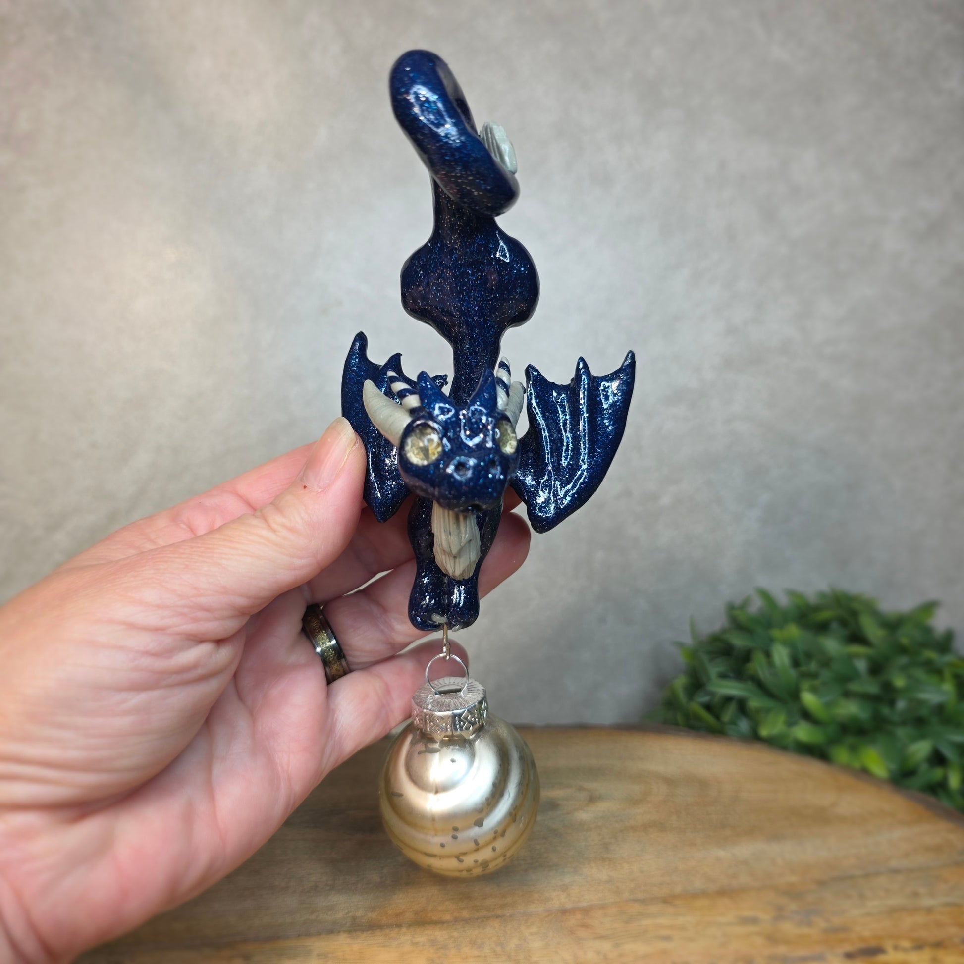 Hand holding a clay dragon with glass ornament against a blurred background