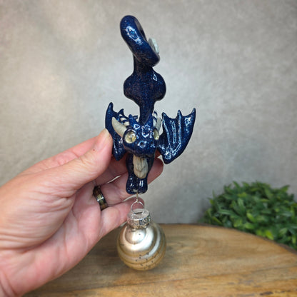 Hand holding a clay dragon with glass ornament against a blurred background