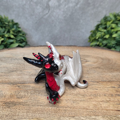 A 2 toned clay dragon sculpture on a wood surface with greenery.