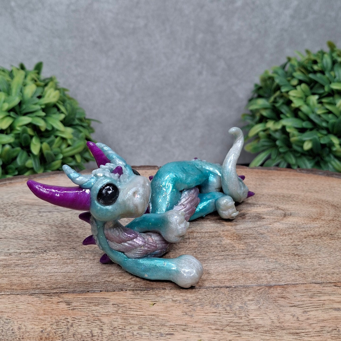 A clay dragon against a wood background with greenery