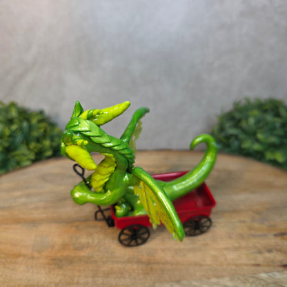 A green clay dragon in a red wagon on a wood surface