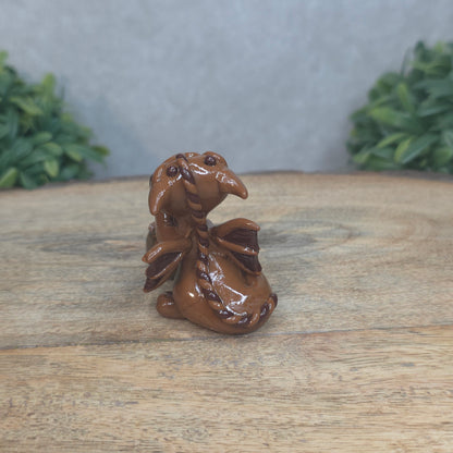 A baby polymer clay dragon with a chocolate truffle against a blurred background