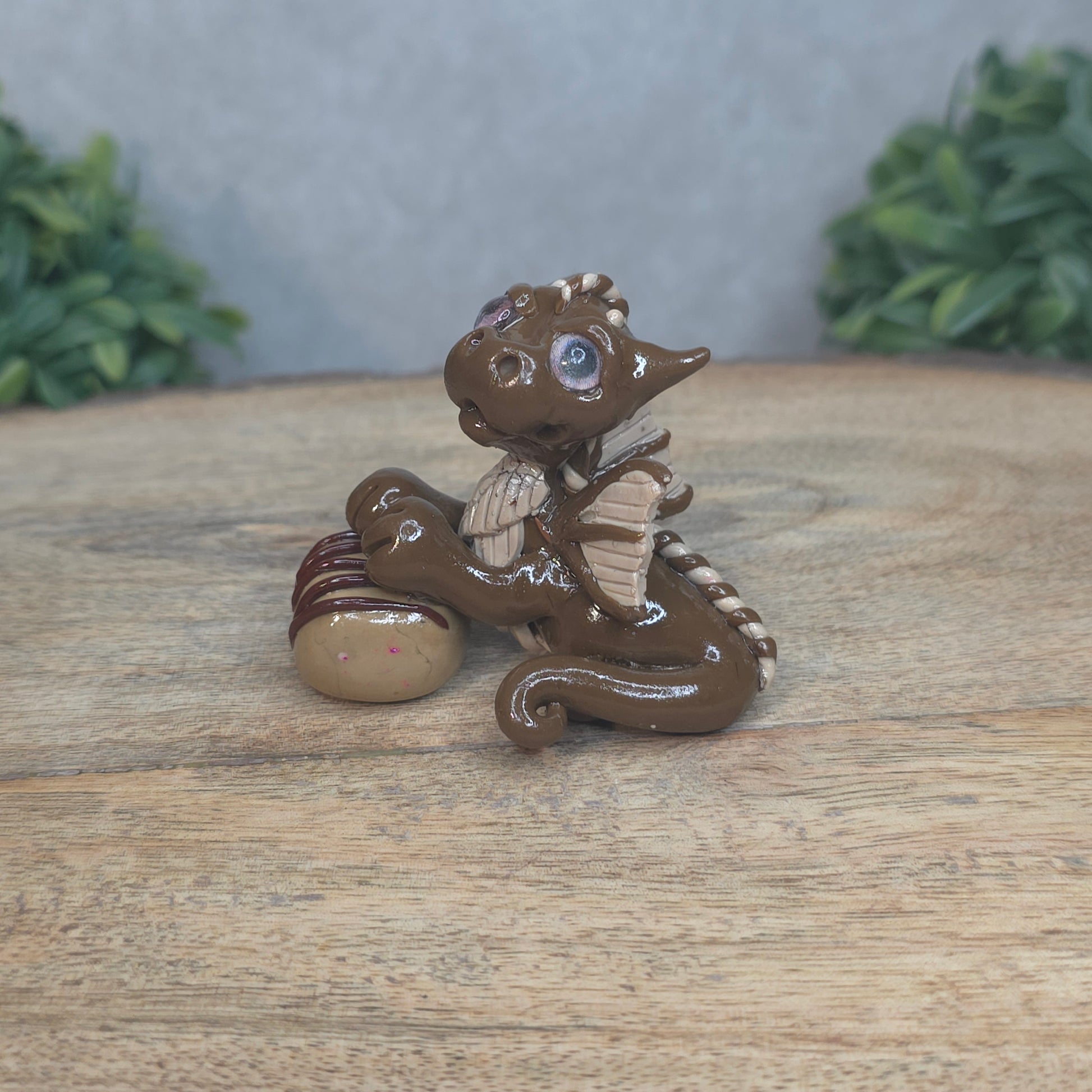 A baby polymer clay dragon with a chocolate truffle against a blurred background